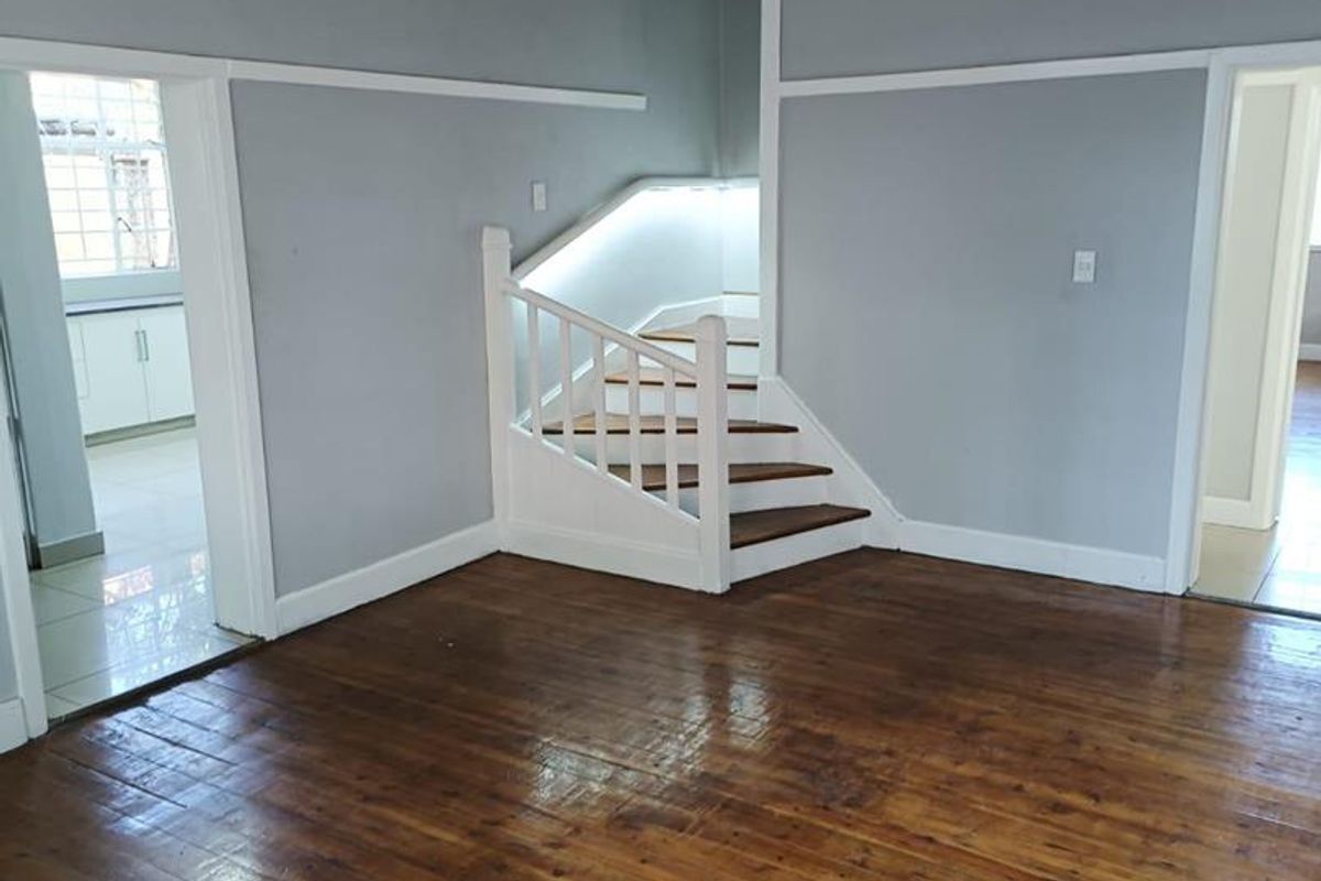 A spacious living area featuring polished timber flooring, high ceilings, and a central staircase with integrated lighting, leading to adjacent rooms.