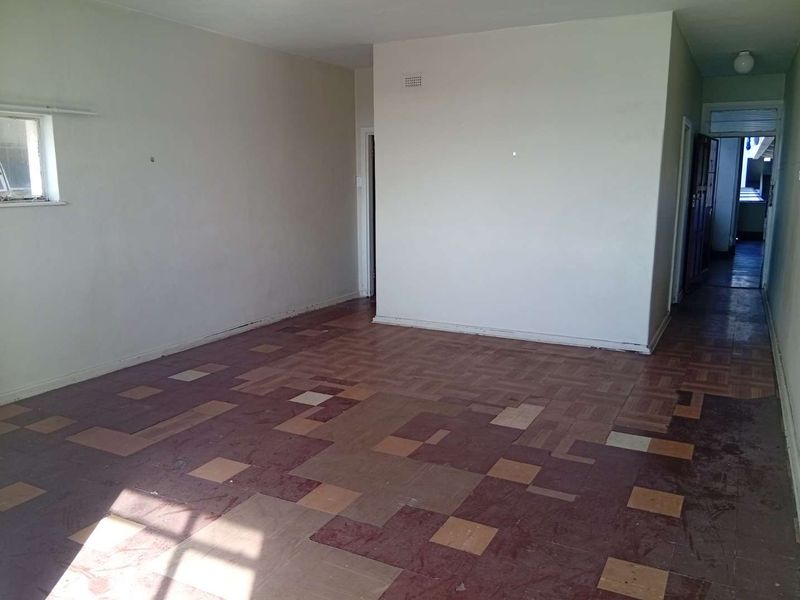 An empty living room featuring original parquet flooring and neutral wall finishes, offering a blank canvas for renovation and interior design updates.