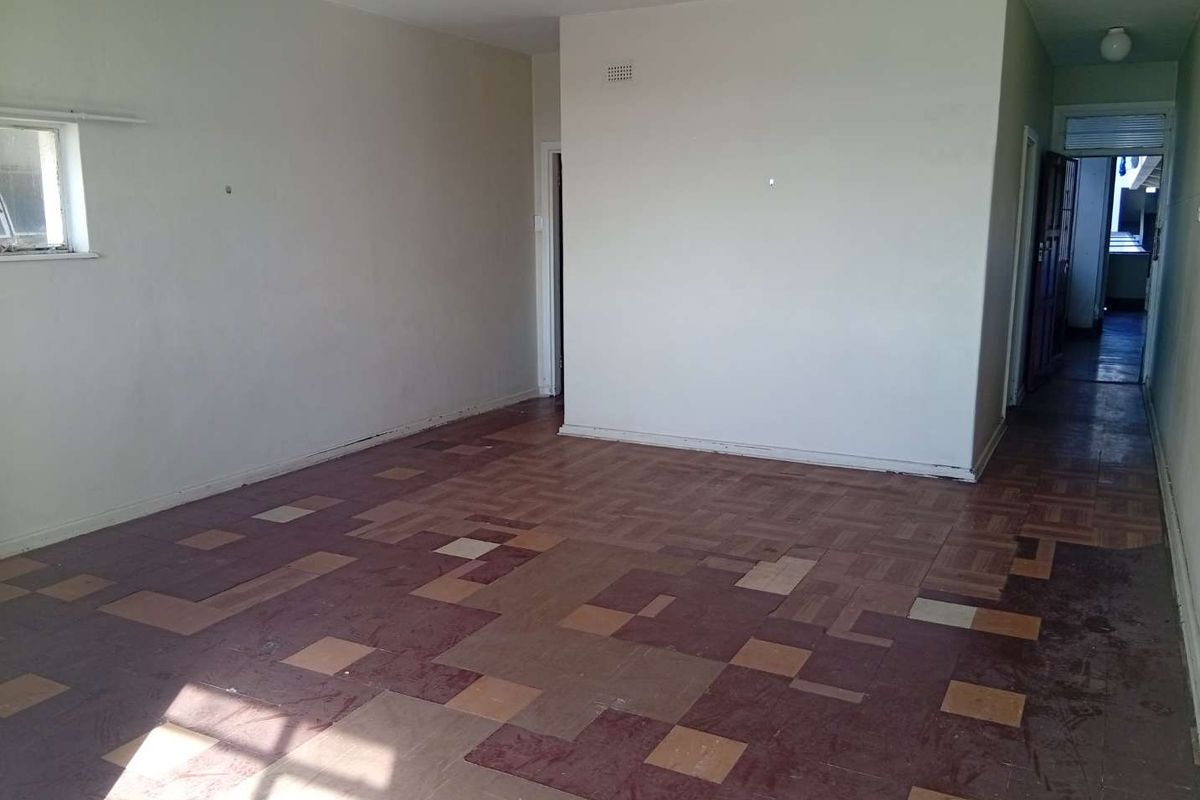 An empty living room featuring original parquet flooring and neutral wall finishes, offering a blank canvas for renovation and interior design updates.