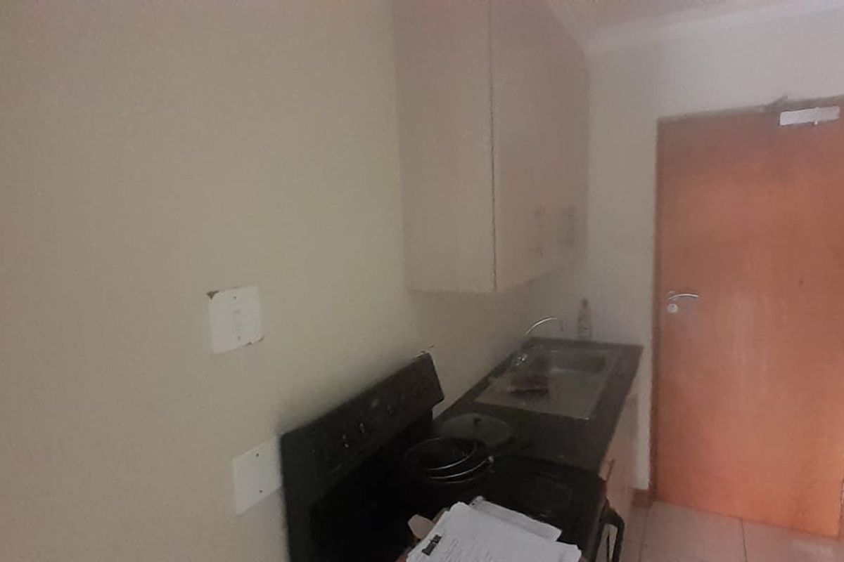 A compact kitchen area featuring built-in cabinetry, a stainless steel sink, and a stove, requiring some cosmetic updates.