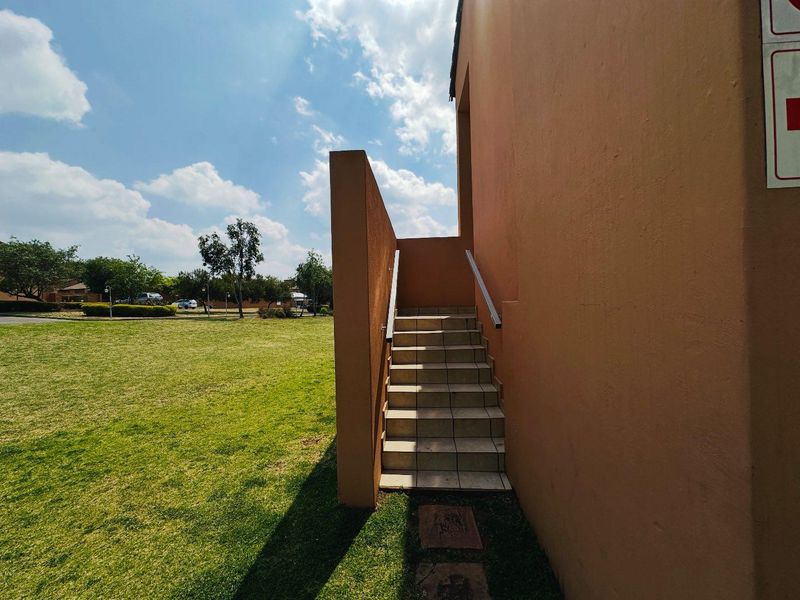 Exterior view of a tiled staircase leading to an upper level, set against a communal garden area with a plastered building facade.