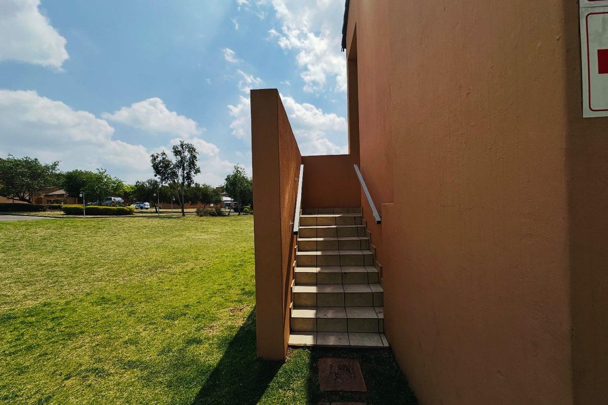 Exterior view of a tiled staircase leading to an upper level, set against a communal garden area with a plastered building facade.