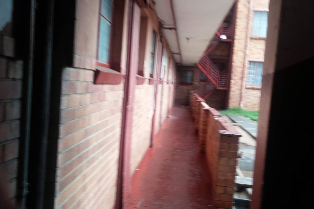 An exterior walkway or corridor in an apartment complex featuring brick walls and a metal staircase in the background.