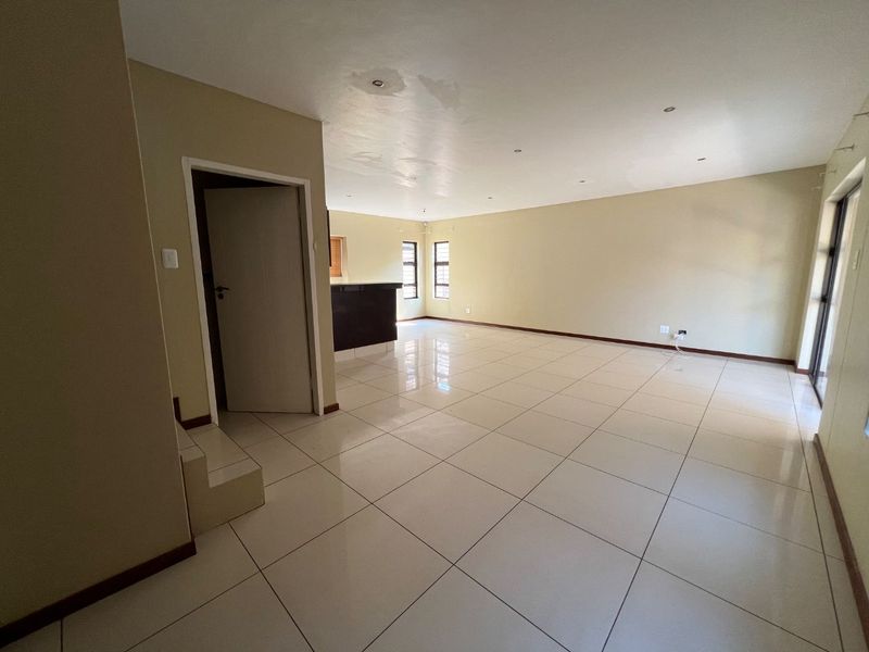 Spacious open-plan living area featuring neutral tiled flooring, recessed lighting, and a breakfast bar, offering a versatile blank canvas for interior design.
