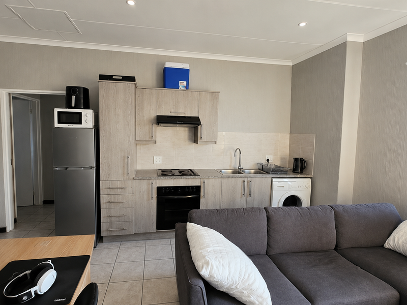Open-plan living area featuring a functional kitchen with built-in cabinetry, integrated appliances, and tiled flooring, seamlessly connected to the lounge space.