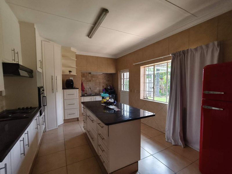 Spacious kitchen featuring a central island with granite countertops, built-in cabinetry, gas hob, and tiled finishes throughout.