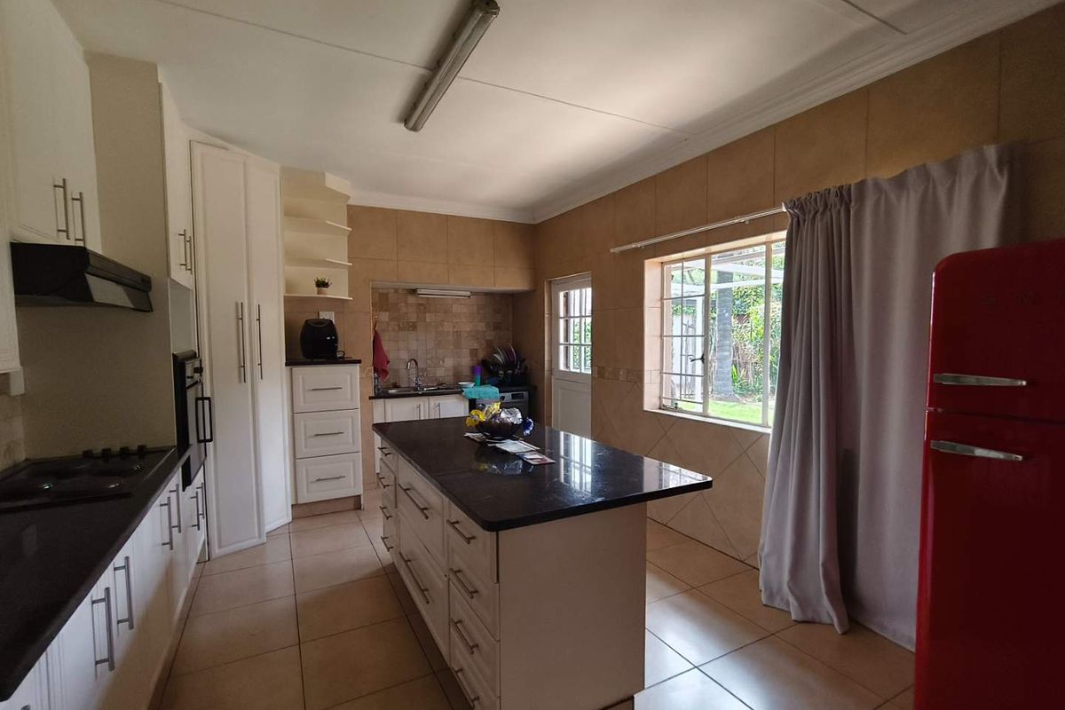 Spacious kitchen featuring a central island with granite countertops, built-in cabinetry, gas hob, and tiled finishes throughout.