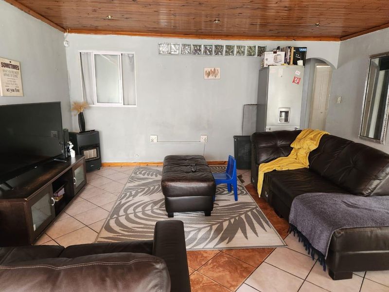 A living room featuring a timber ceiling, tiled flooring, and a glass block window, offering a functional space with potential for cosmetic updates.