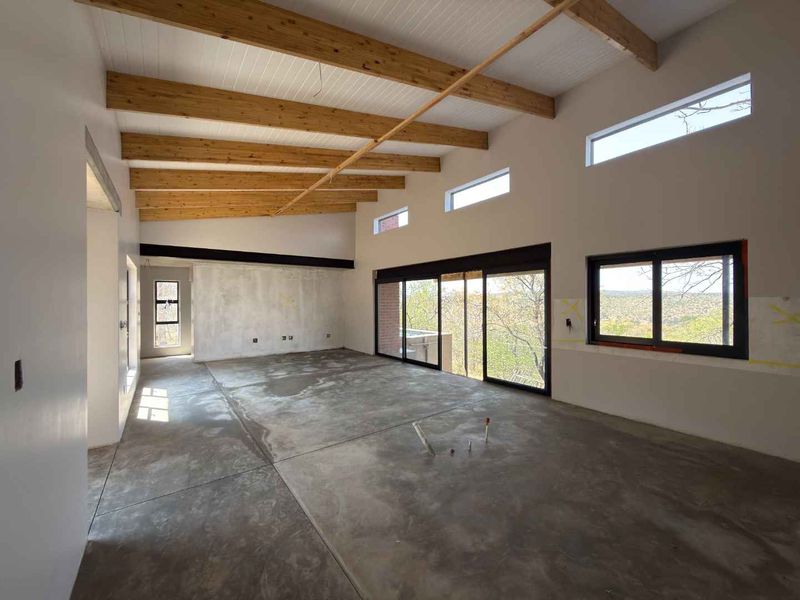 Spacious open-plan living area featuring exposed timber beams, high ceilings, clerestory windows, and large sliding doors leading to an outdoor view.