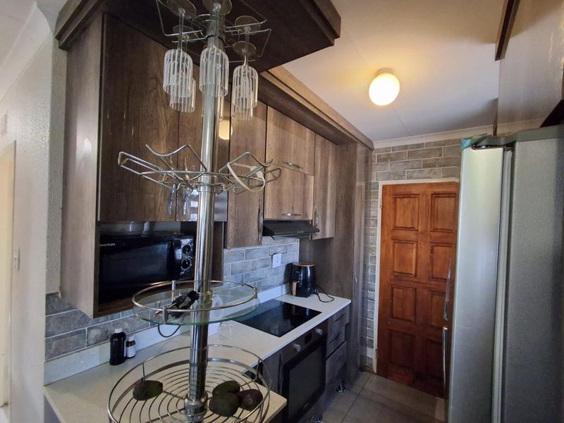A functional kitchen featuring wood-finish cabinetry, stone countertops, a built-in electric hob and oven, and a decorative tiled backsplash.