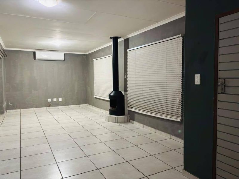Spacious living area featuring tiled flooring, a modern freestanding fireplace, and a wall-mounted air conditioning unit, offering a clean and neutral blank canvas.