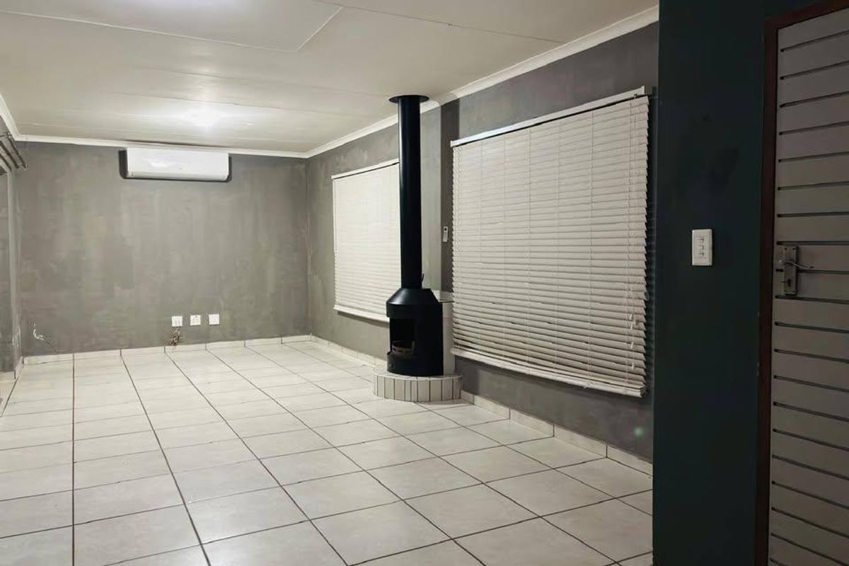 Spacious living area featuring tiled flooring, a modern freestanding fireplace, and a wall-mounted air conditioning unit, offering a clean and neutral blank canvas.