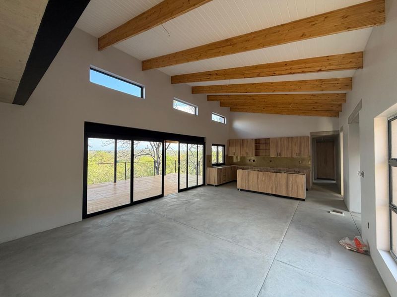 Spacious open-plan living and kitchen area featuring polished concrete floors, exposed timber beams, and large sliding doors opening onto a wooden deck.