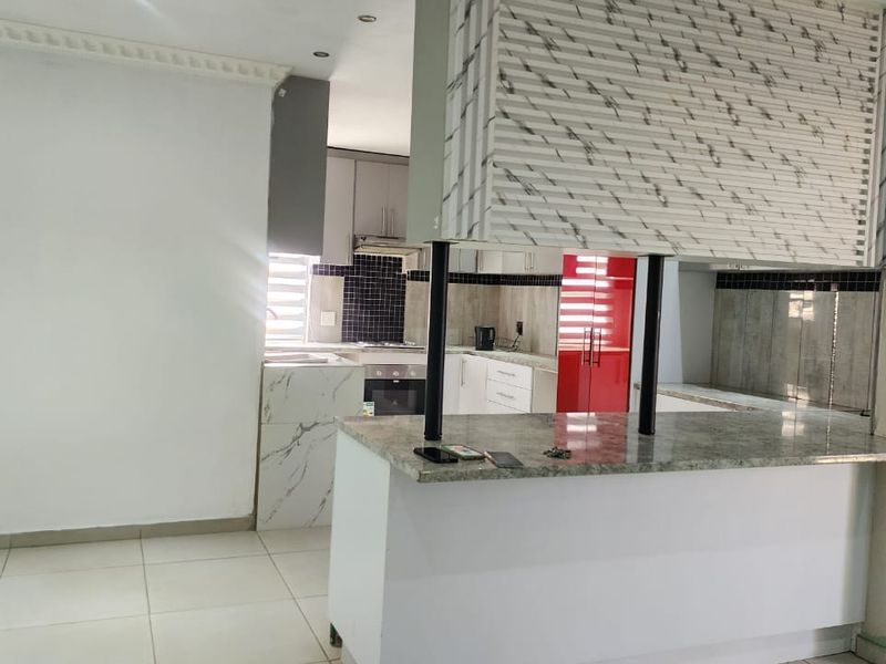 Open plan kitchen featuring a granite breakfast bar, built-in oven, hob, and extractor fan, with tiled flooring throughout the living area.