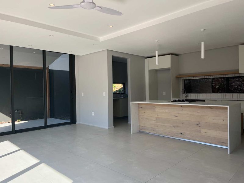 Modern open-plan living area featuring a sleek kitchen with a timber-accented island, gas hob, and large sliding doors leading to the outdoor space.