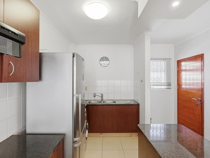 A functional kitchen featuring dark wood cabinetry, granite countertops, a double bowl sink, and tiled flooring with a clean, neutral aesthetic.