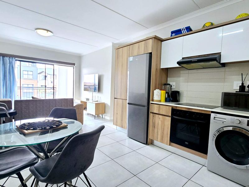 Modern open-plan living area featuring a contemporary kitchen with built-in appliances, tiled flooring, and seamless access to a balcony through sliding glass doors.