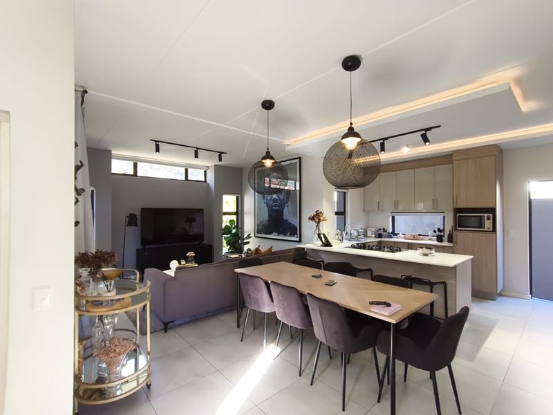 Modern open-plan living area featuring a sleek kitchen with island, gas hob, built-in appliances, and contemporary lighting, seamlessly flowing into the dining and lounge space.