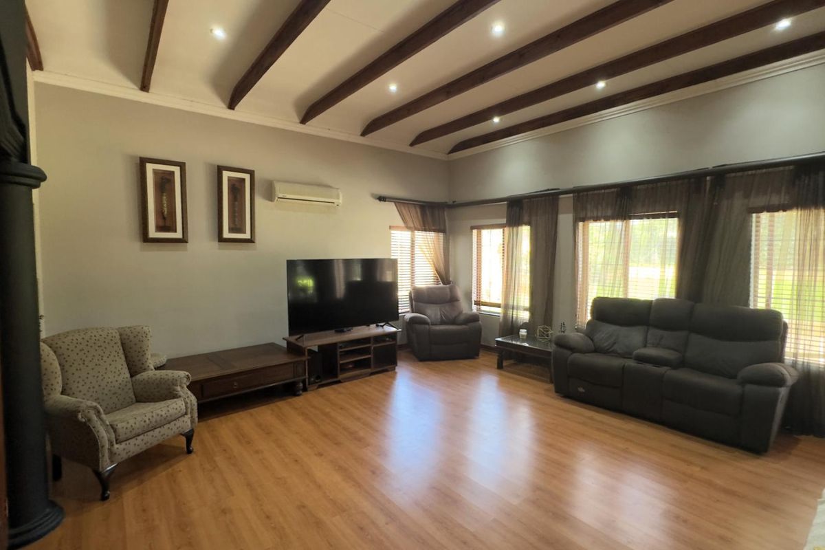Spacious living room featuring high vaulted ceilings with exposed timber beams, recessed downlighting, laminate wood flooring, and a wall-mounted air conditioning unit.