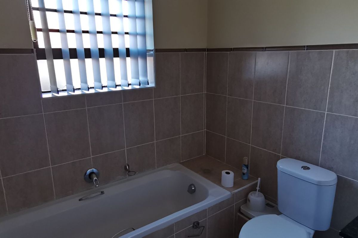 A functional bathroom featuring a built-in bathtub, tiled walls, a standard toilet, and a vanity basin with a window providing natural light.