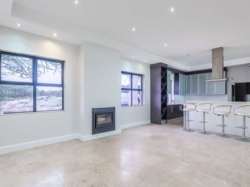 Spacious open-plan living and kitchen area featuring modern cabinetry, a built-in fireplace, stone tile flooring, and recessed lighting throughout.