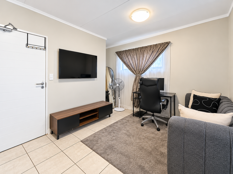 A functional office space featuring tiled flooring, neutral wall finishes, and a window with curtain treatments.