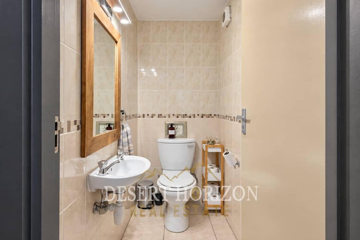 A compact, well-maintained bathroom featuring tiled walls and flooring, a wall-mounted basin, and a standard toilet.