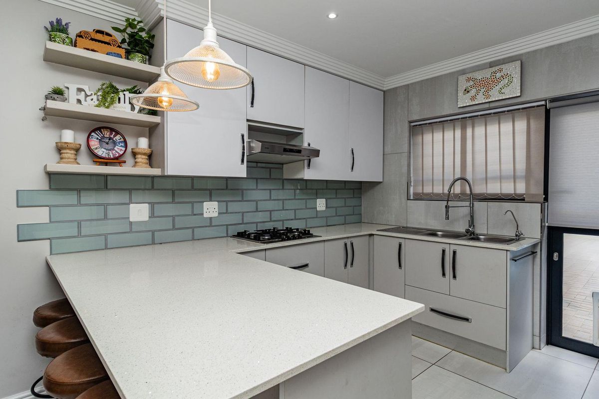 Modern kitchen featuring light grey cabinetry, stone countertops, a gas hob, extractor fan, and a stylish subway tile backsplash.