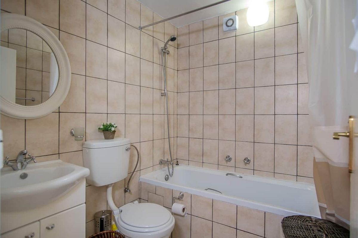 A functional bathroom featuring a standard bathtub with shower attachment, pedestal vanity, and toilet, finished with neutral wall tiles.