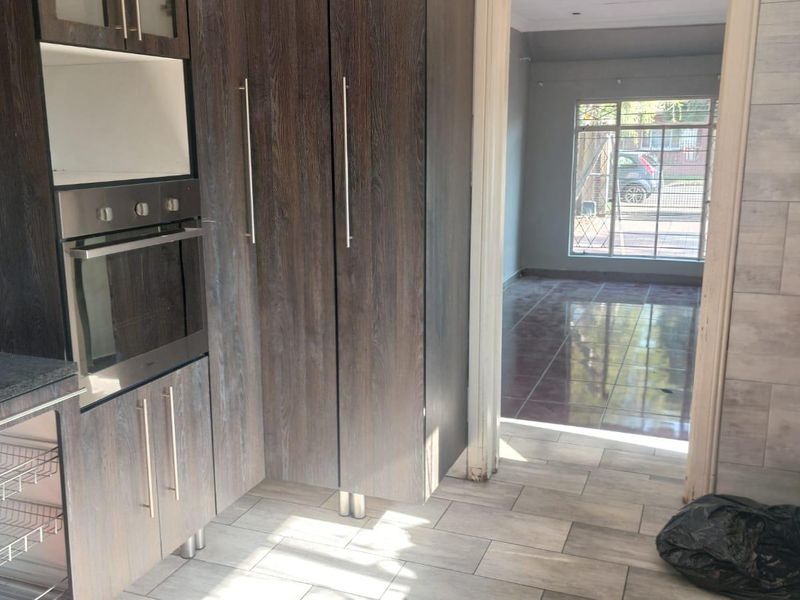 A modern kitchen featuring dark wood-grain cabinetry, built-in oven, and granite countertops, leading into an adjacent tiled living area.