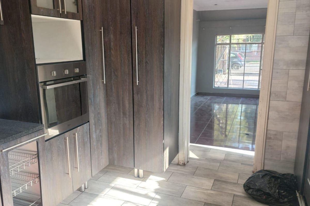A modern kitchen featuring dark wood-grain cabinetry, built-in oven, and granite countertops, leading into an adjacent tiled living area.