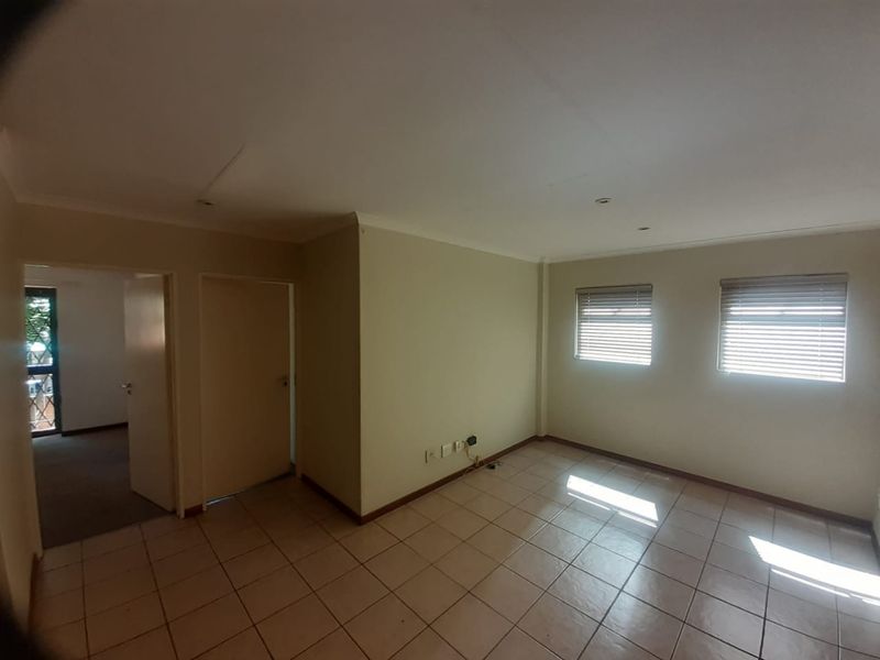 An empty living room featuring tiled flooring, recessed downlights, and venetian blinds, offering a neutral blank canvas for potential interior design updates.