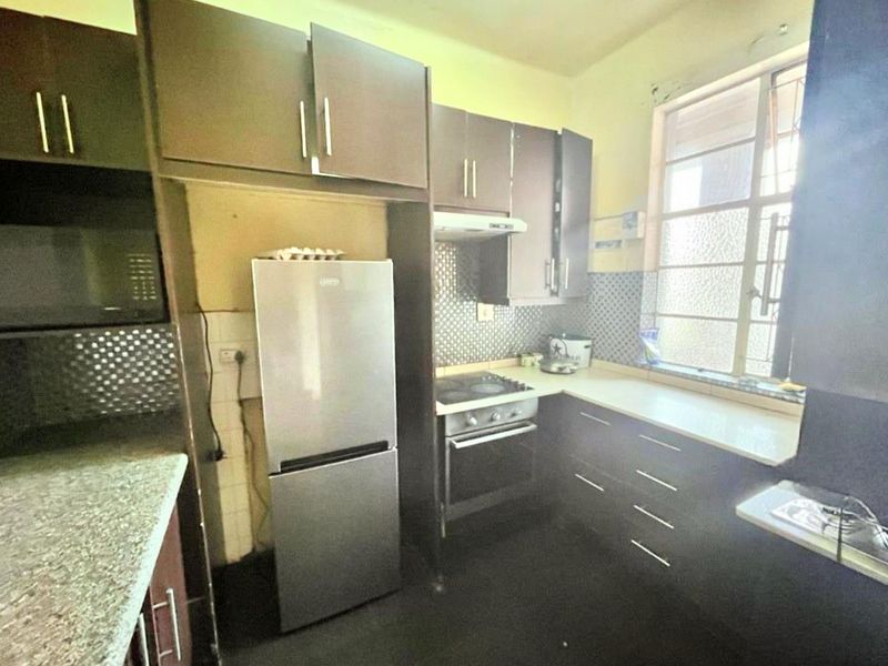 A compact kitchen featuring dark built-in cabinetry, laminate countertops, an electric stove with extractor fan, and a tiled backsplash.