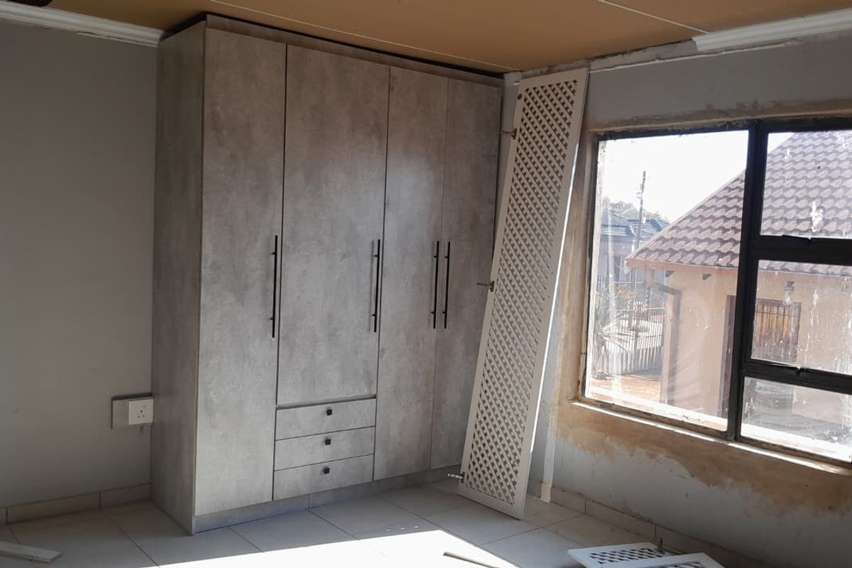 Bedroom featuring modern built-in cupboards and tiled flooring, currently undergoing finishing touches around the window and ceiling area.