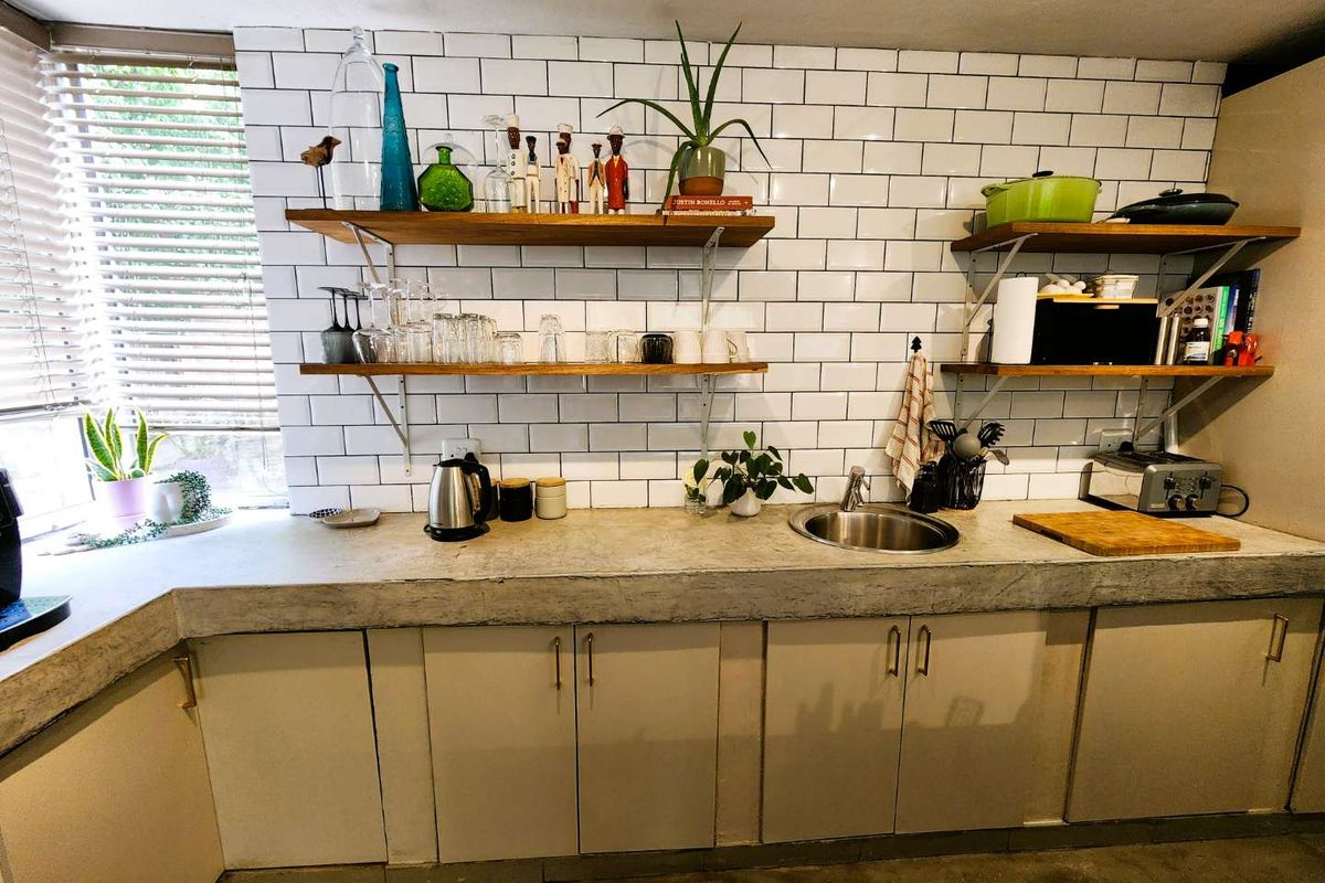 Kitchen area featuring white subway tile backsplash, open timber shelving, concrete countertop, and stainless steel sink.