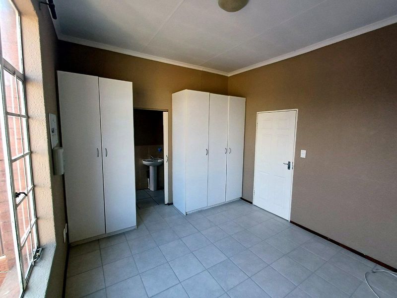 A spacious bedroom featuring tiled flooring, built-in cupboards, and an en-suite area with a pedestal basin.