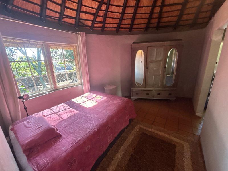 A bedroom featuring a traditional thatched roof, terracotta tile flooring, and leaded glass windows, offering a rustic cottage aesthetic.