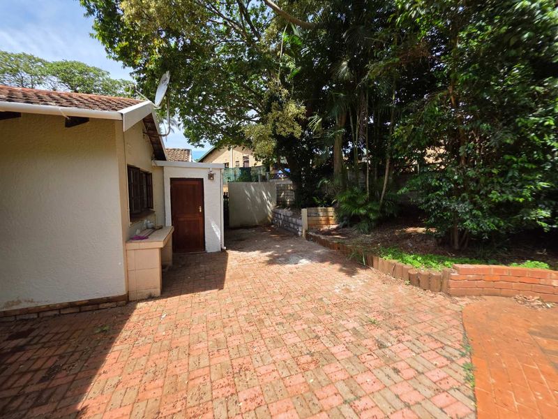 Rear exterior area featuring brick paving, a built-in outdoor counter, and established garden landscaping with a retaining wall.