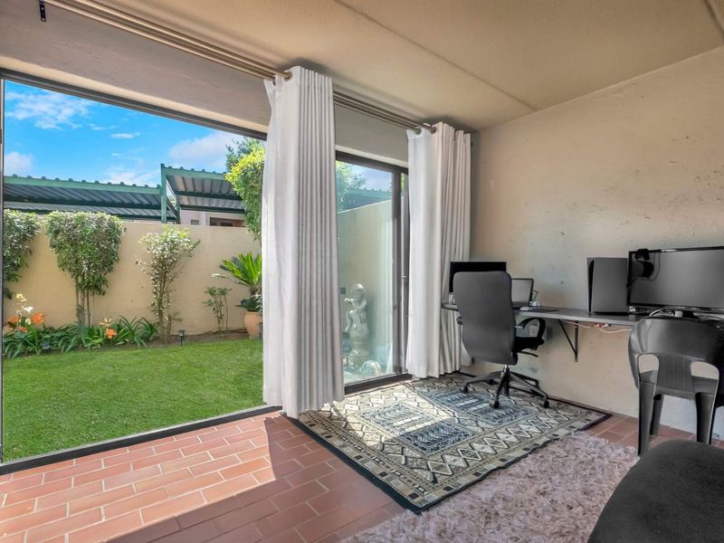 A functional home office space featuring terracotta tile flooring and large sliding glass doors that provide direct access to a private garden area.