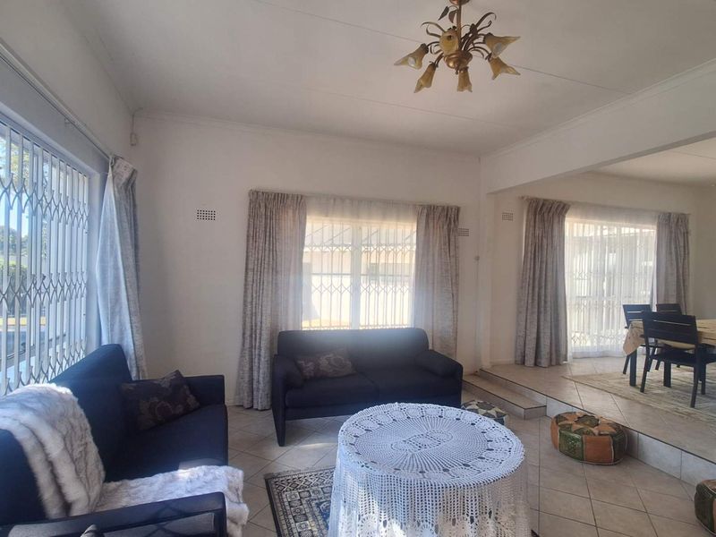 Spacious open-plan living and dining area featuring tiled flooring, security gates on windows, and a raised dining section.