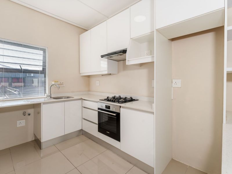 Modern kitchen featuring white cabinetry, stone countertops, built-in oven, gas hob, extractor fan, and tiled flooring.