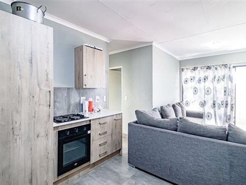 Open-plan living area featuring a modern kitchenette with built-in oven, hob, and light wood-finish cabinetry, seamlessly flowing into the lounge space.