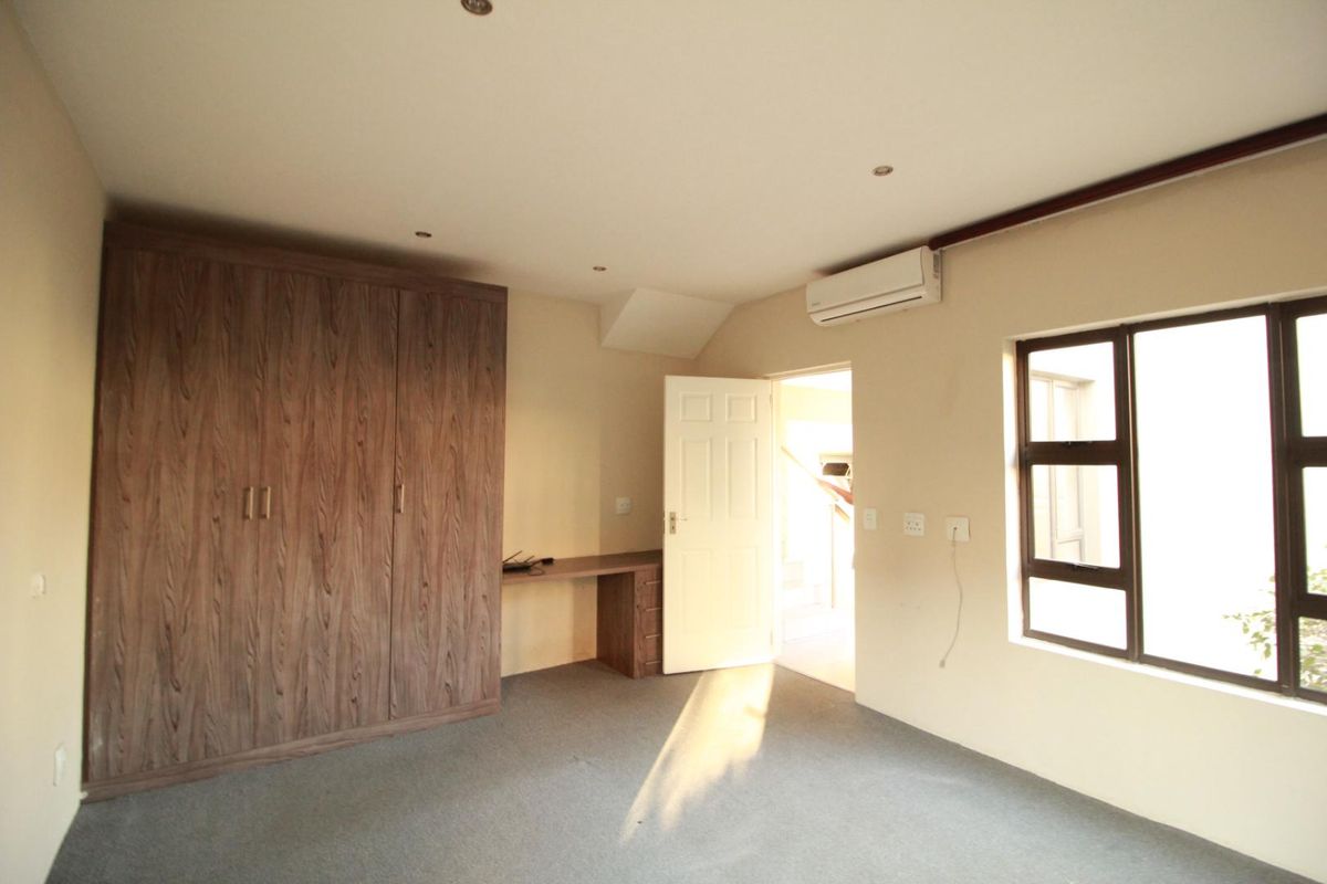 A spacious bedroom featuring built-in wooden cabinetry, a integrated desk, split-system air conditioning, and neutral carpeting.