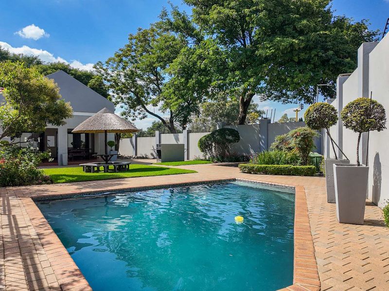 A well-maintained outdoor pool area featuring a paved patio, a thatched lapa, and secure perimeter walling with electric fencing.