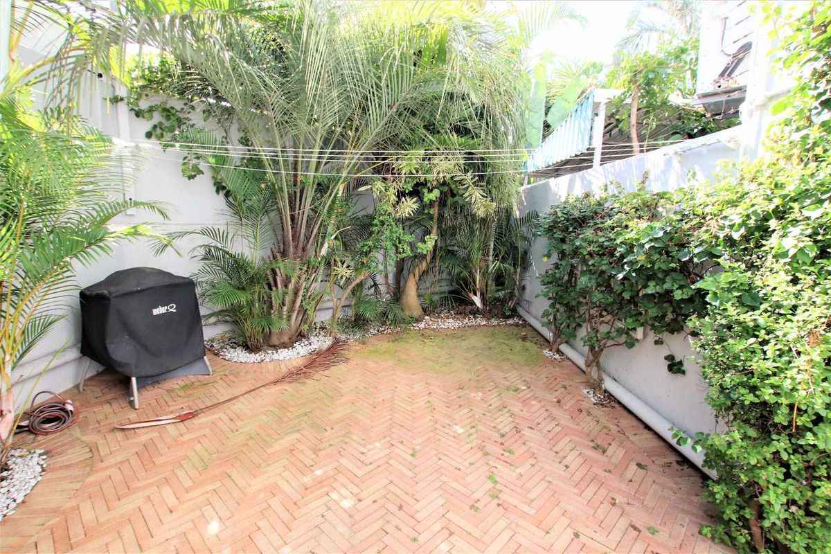 A private rear courtyard featuring herringbone brick paving, perimeter boundary walls, and established garden landscaping.