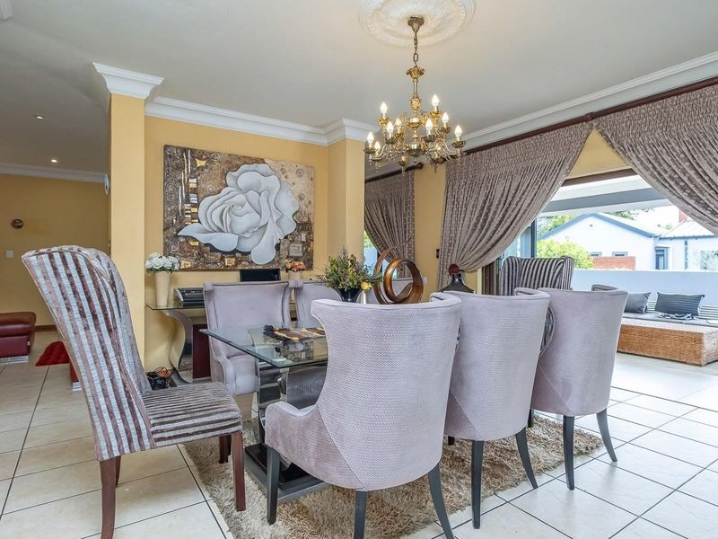 A formal dining room featuring tiled flooring, decorative ceiling rose with a chandelier, and large sliding glass doors leading to an outdoor patio area.