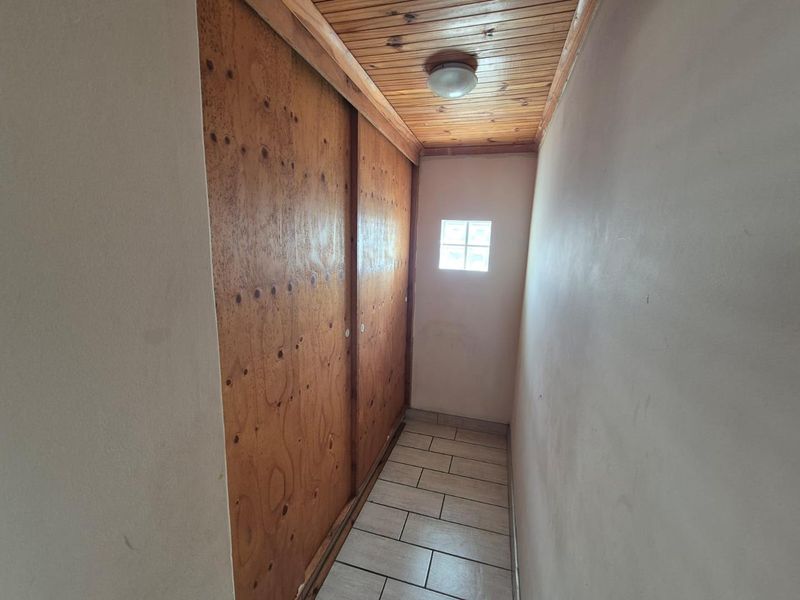 A narrow hallway featuring tiled flooring, a timber-paneled ceiling, and built-in sliding wooden cupboard doors.