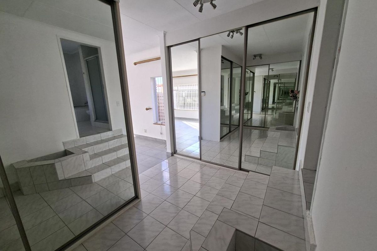 Spacious bedroom featuring large mirrored sliding wardrobes, tiled flooring, and a raised tiled platform area.