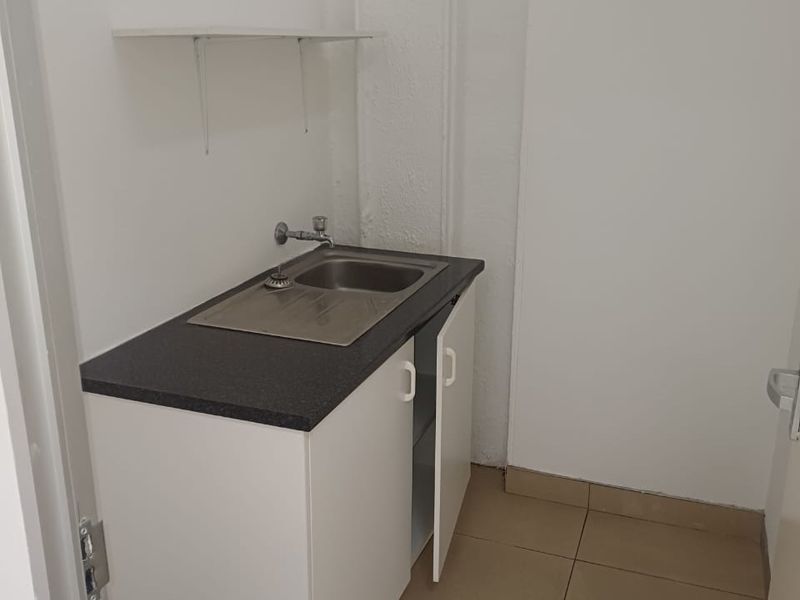 A compact utility space featuring a stainless steel sink, laminate countertop, base cabinetry, and tiled flooring.