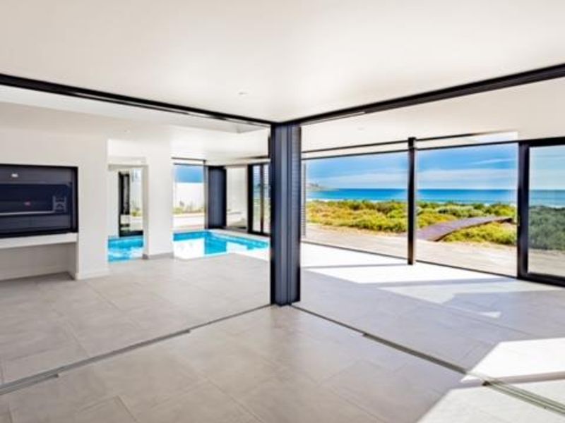 Modern covered patio featuring a built-in braai, tiled flooring, and seamless sliding glass doors opening to a swimming pool and coastal views.